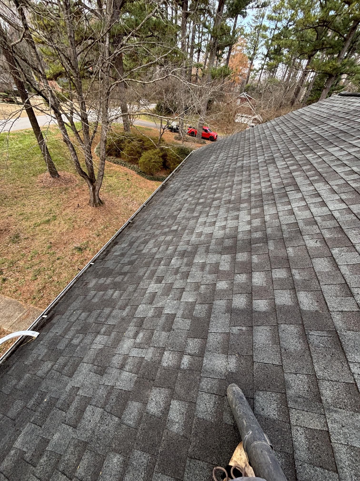 A close up of a roof with a gutter and trees in the background.