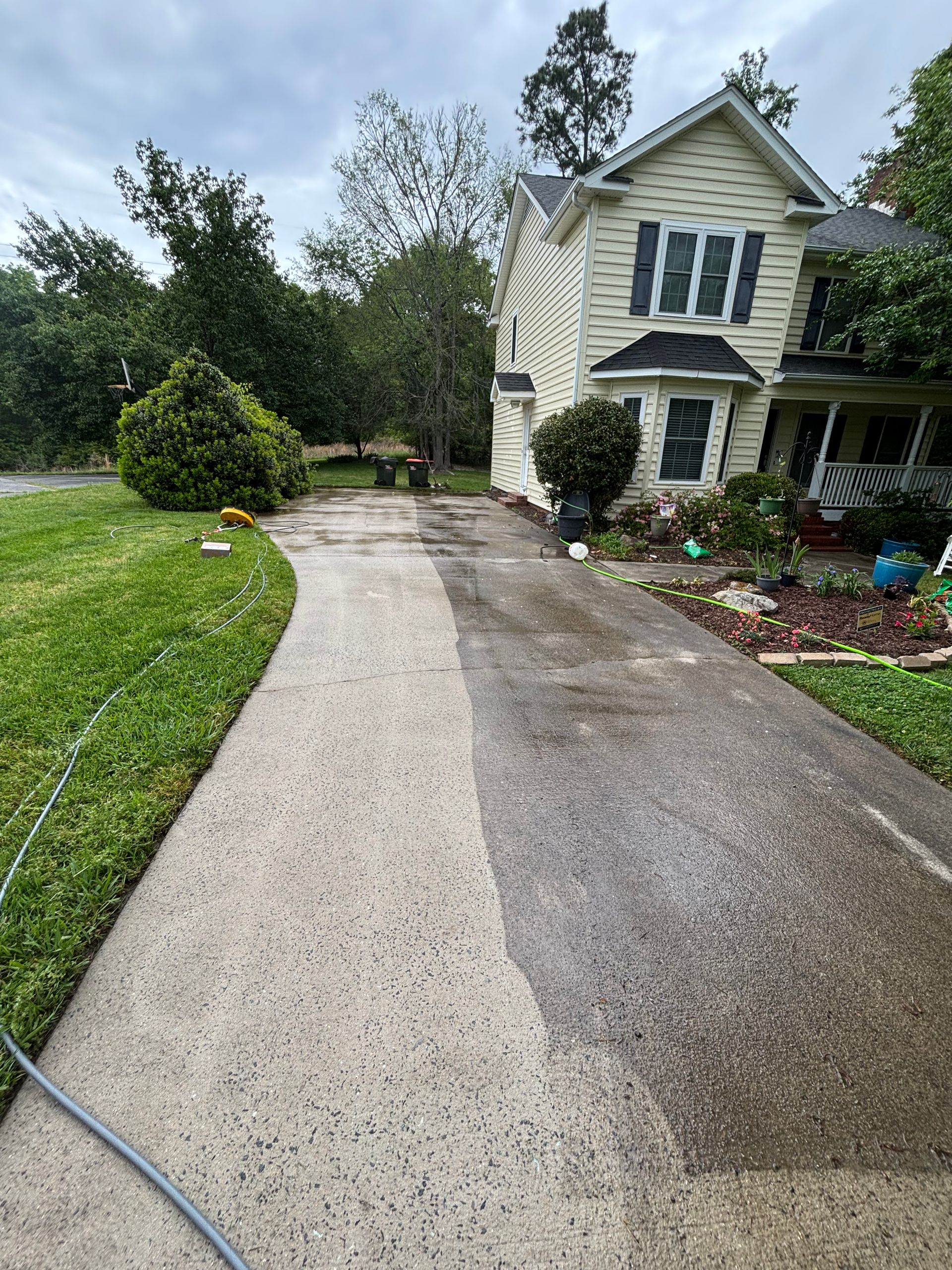 Driveway being pressure washed; half is clean, half is dirty. House and green lawn are visible.
