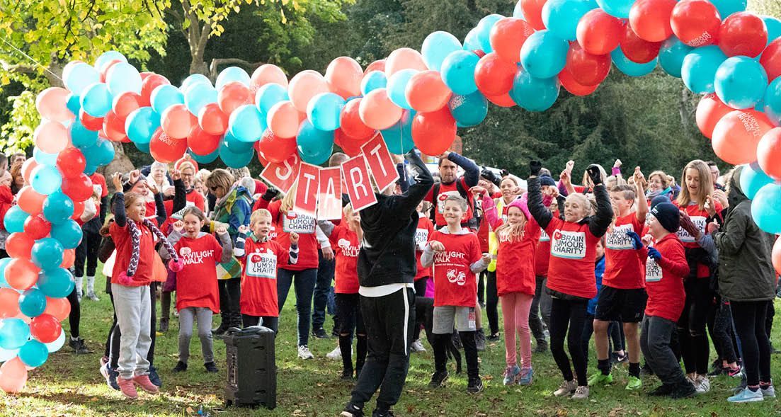 People at a running event under a balloon arch, many wearing red shirts, cheering.