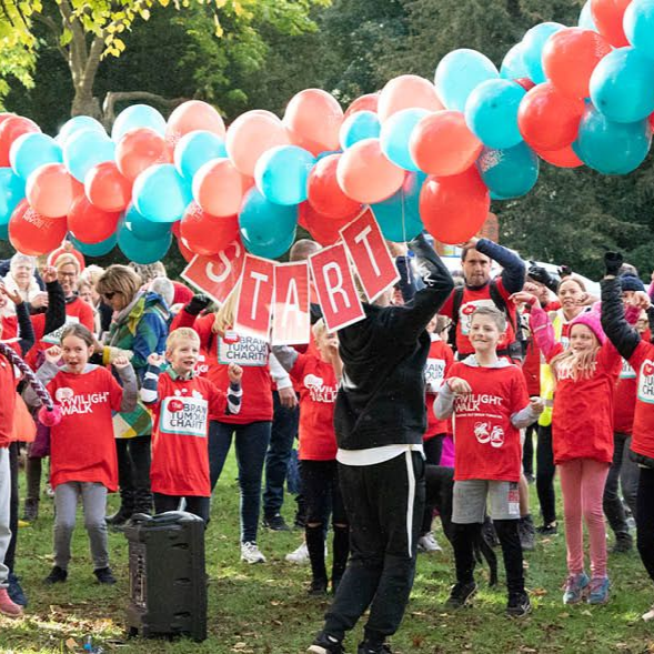 Children in red shirts cheer at a starting line, under balloons and a 