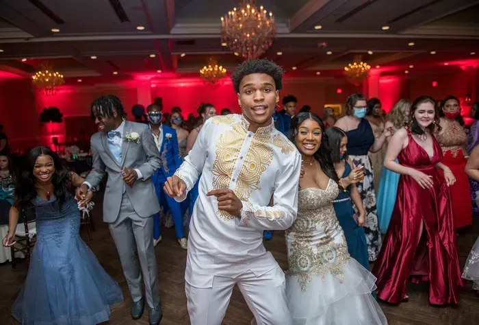 People dancing joyfully at a prom, illuminated with red lighting.