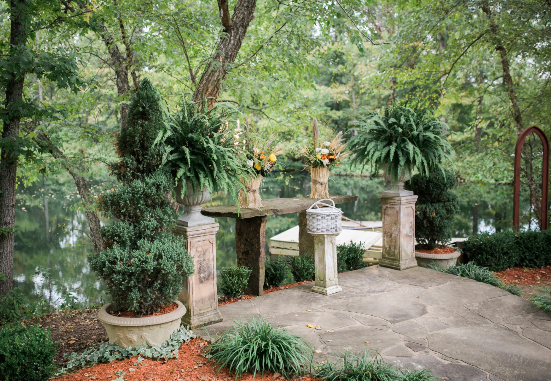 Garden entrance with stone pillars, potted plants, and a leafy path under trees