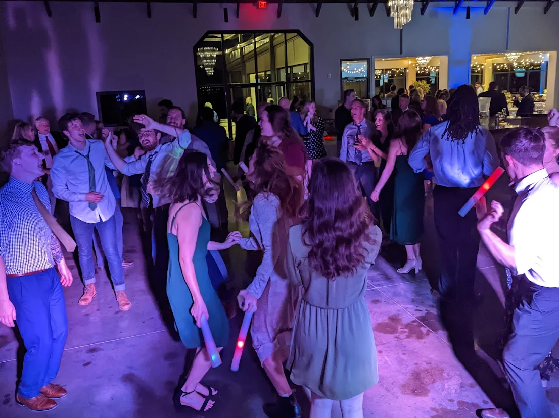 People dancing at a crowded indoor party with purple lighting and glow sticks