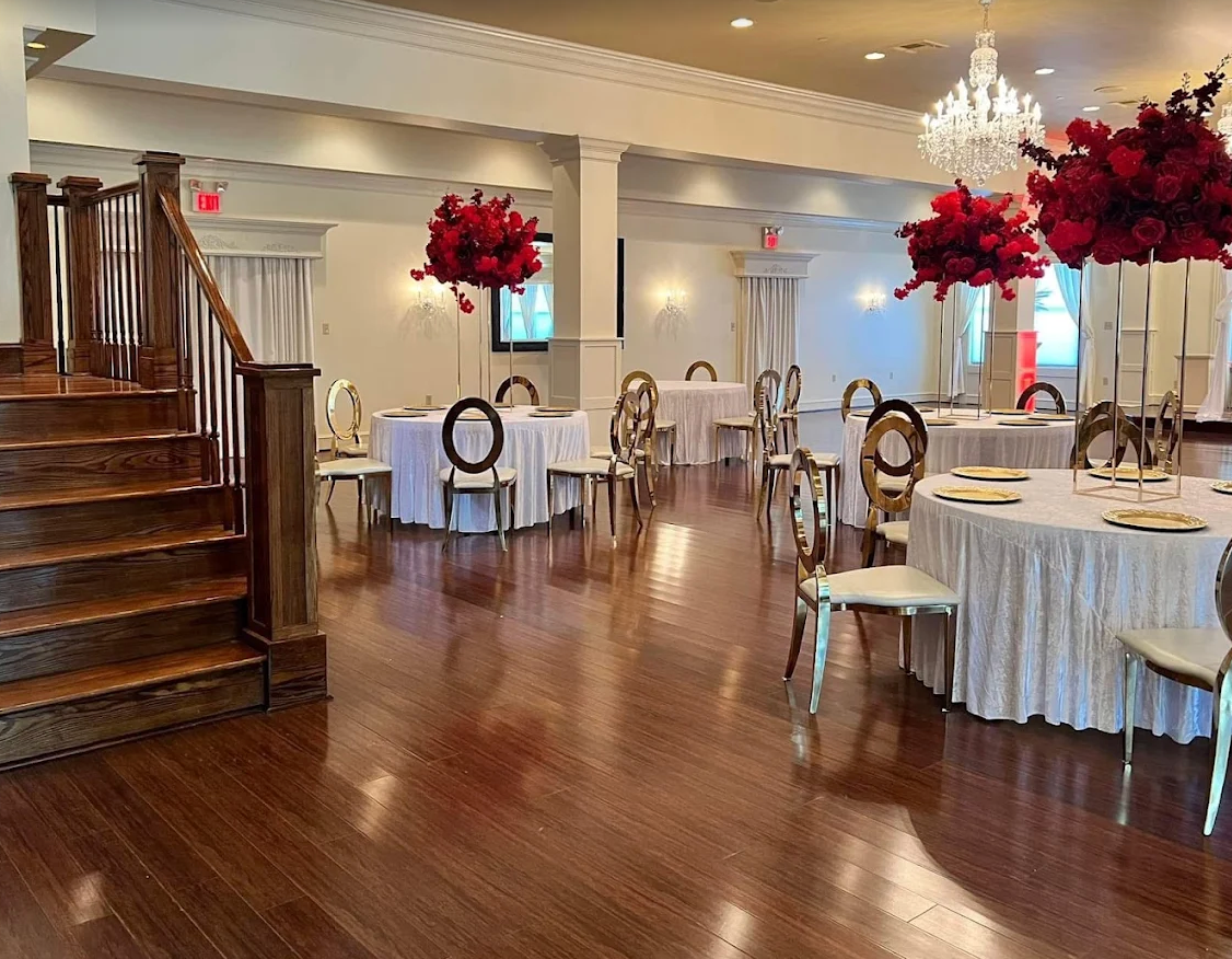 Elegant banquet hall with polished wood floors, round tables, and red floral centerpieces beside a staircase