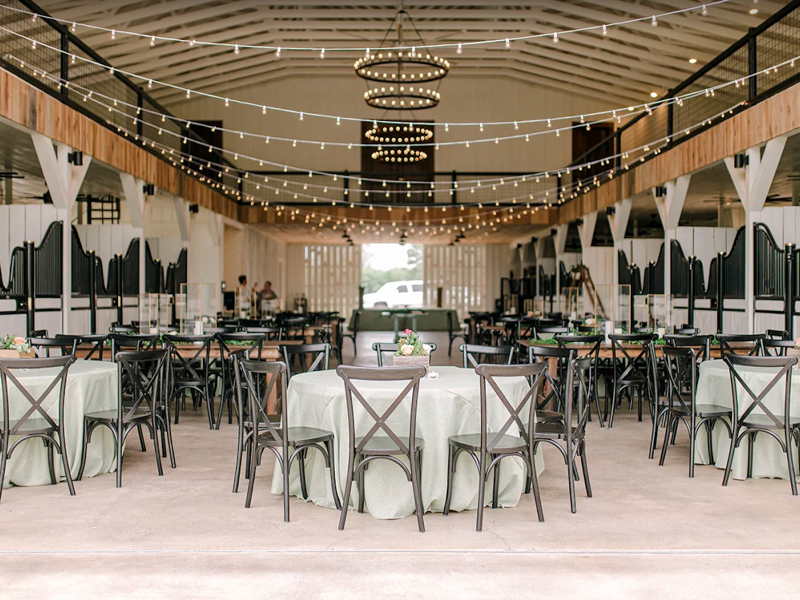 Elegant indoor dining hall with white chairs, green plants, and hanging lights under a wooden ceiling