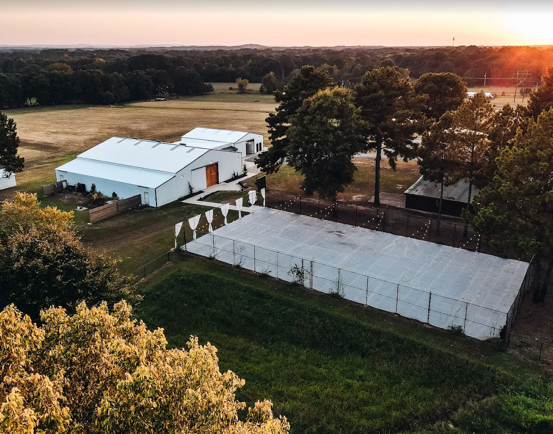 Aerial view of two white event tents beside trees and fields at sunset.