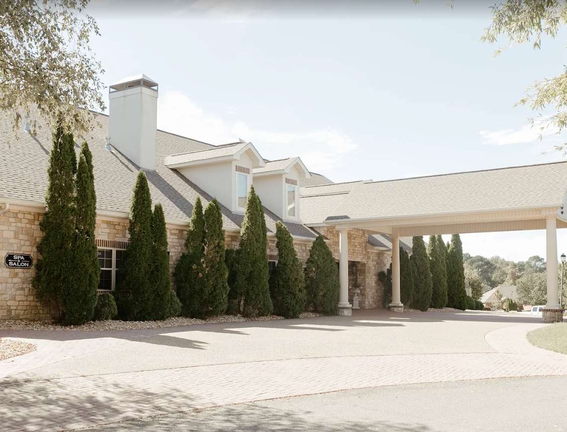 White stucco house with a covered driveway, tall cypress trees, and a bright desert landscape