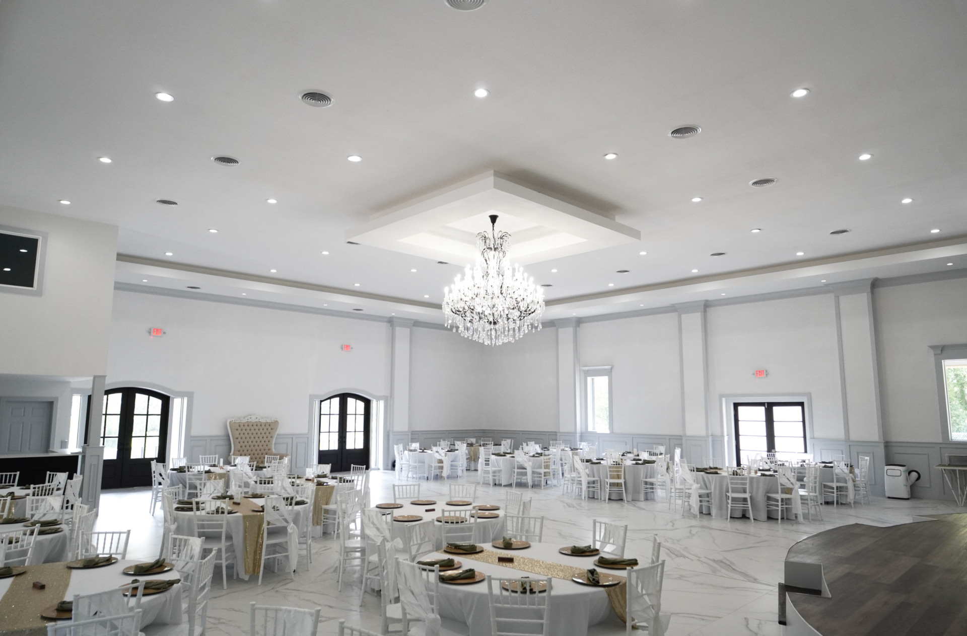 Elegant white banquet hall with chandeliers, round tables, and chairs set for an event