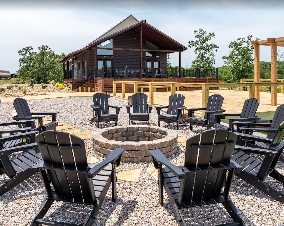 Outdoor cabin with a stone fire pit and black chairs on a gravel patio