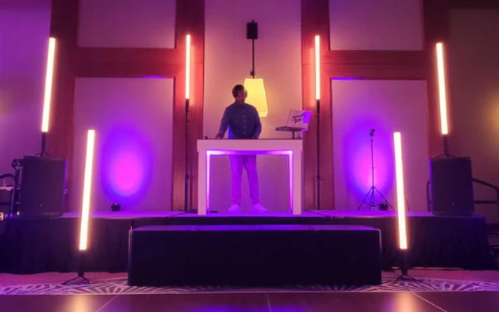DJ performing on a purple-lit stage with speakers and a white table in the center