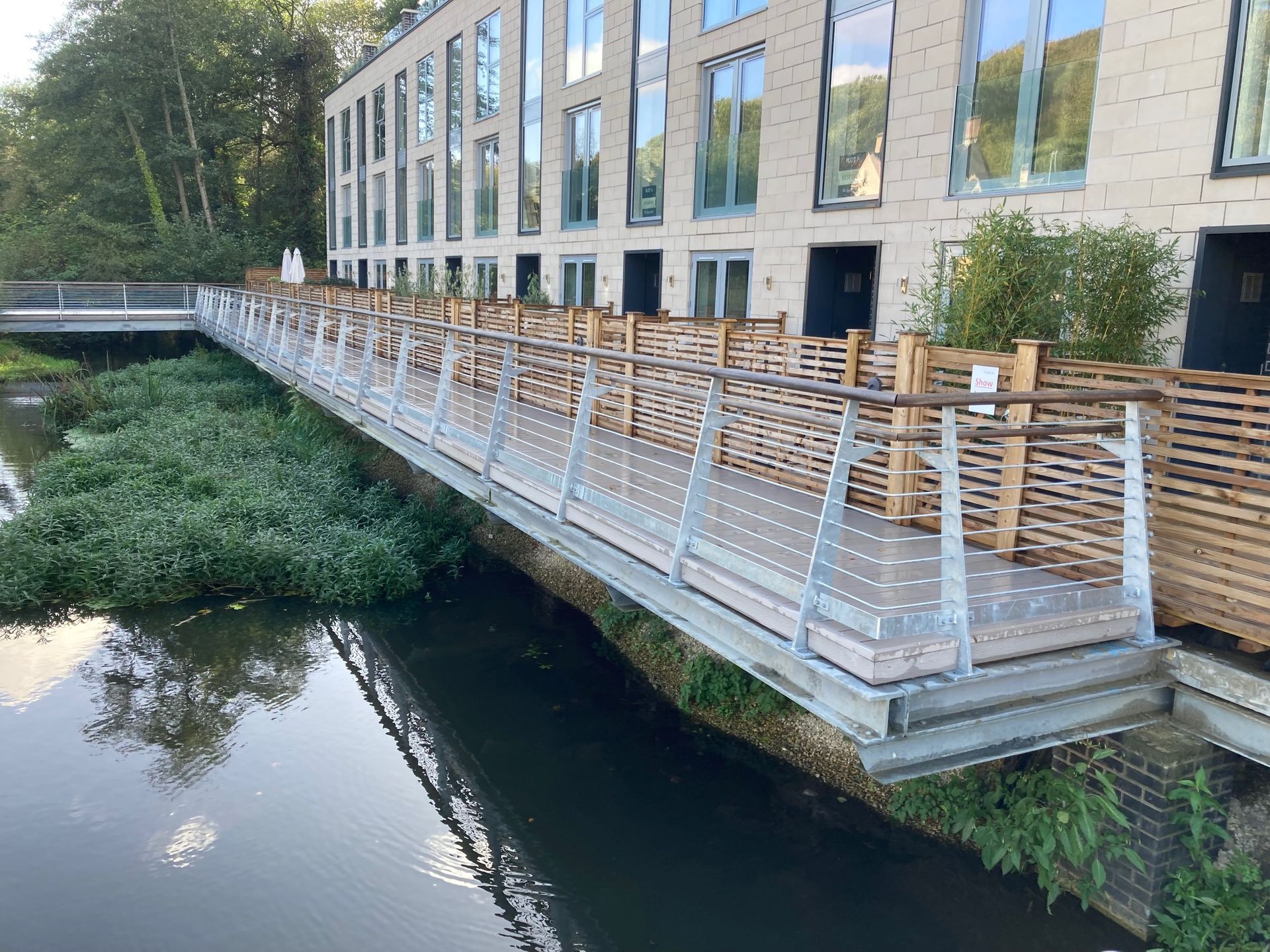 Bridge over water with building, light brick facade, wooden and metal railings.