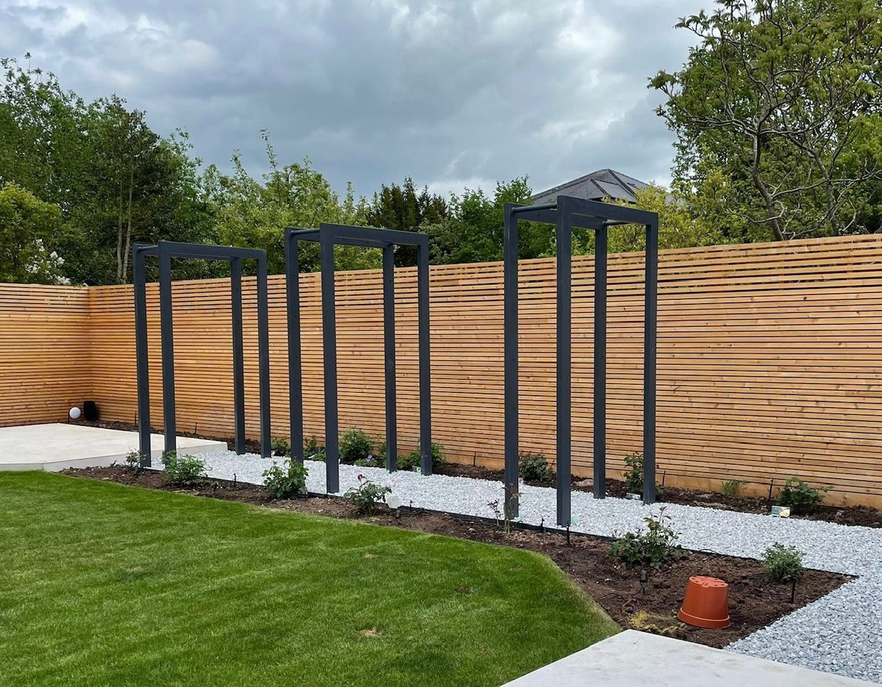 Modern garden with dark gray metal frames, wood fence, gravel path, and green lawn.