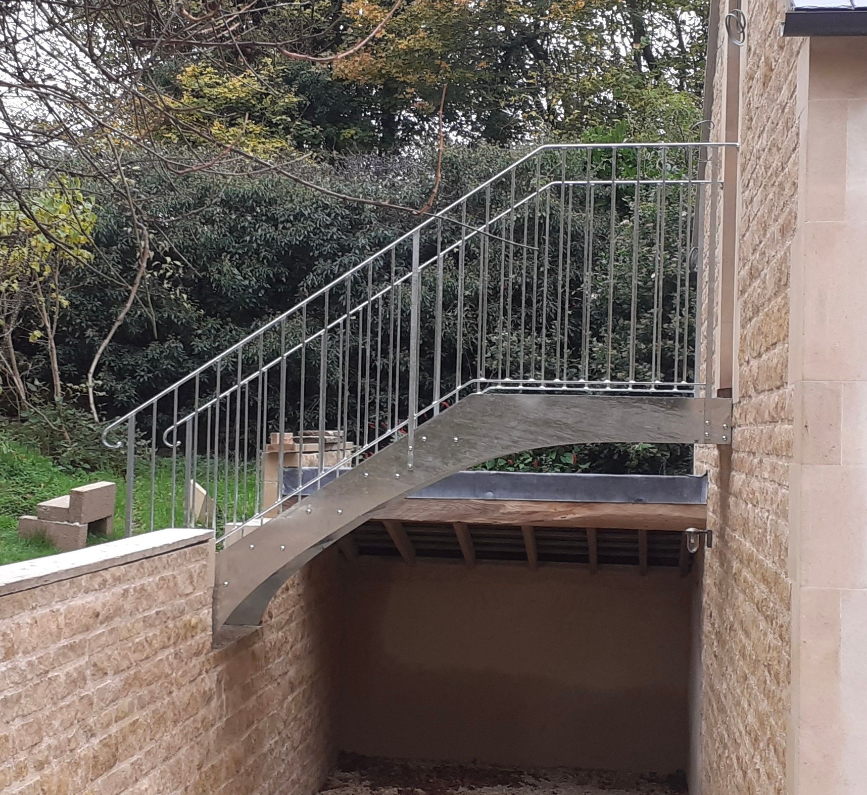 Metal staircase with railing ascending beside a stone building, leading to a wooden platform.