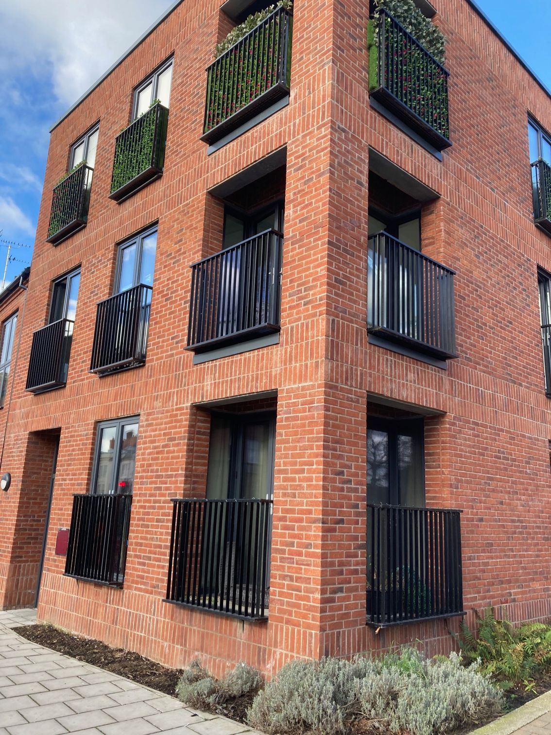 Red brick apartment building with black metal balconies and windows.