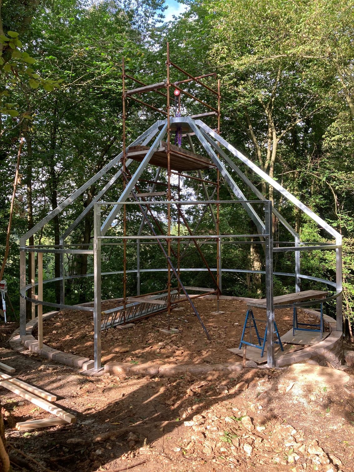 Metal frame of a building under construction, in a forest setting.