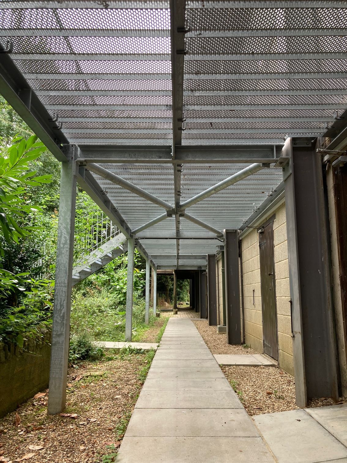 Long hallway with concrete path, metal roof and supports, and stone walls.