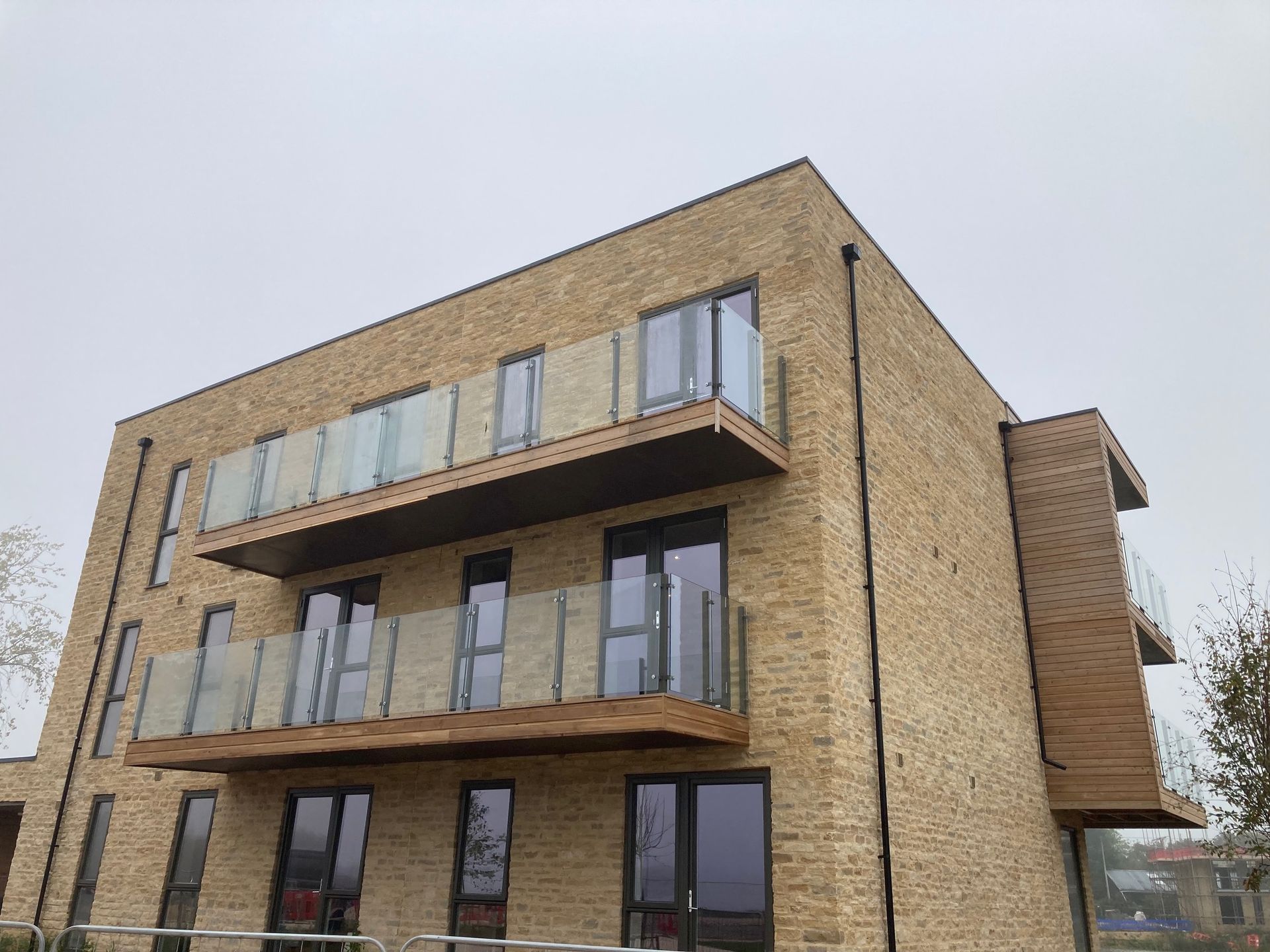 Tan brick apartment building with glass balconies against a gray sky.