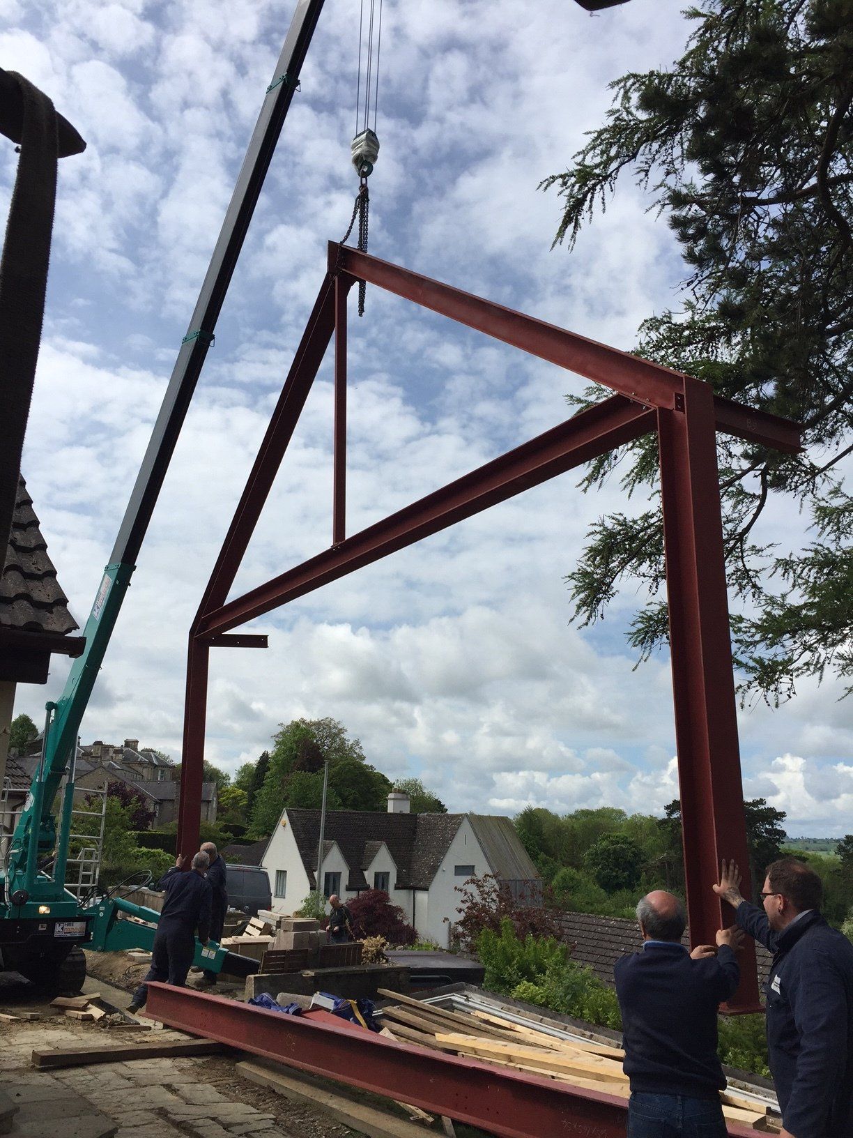 Crane lifting red steel frame for construction near houses.
