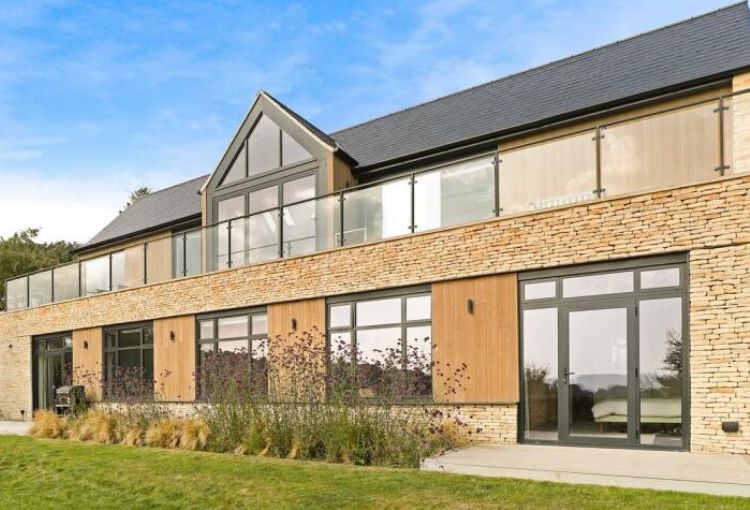 Modern two-story house with glass balconies, tan brick exterior, and dark roof . Cotwsold stone house.