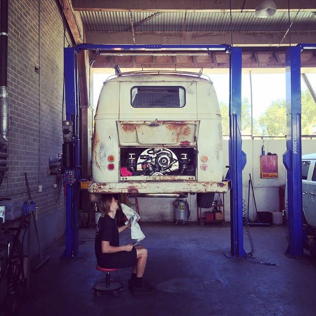 A Man Sits on a Stool in Front of a White Van on a Lift — Stokers VW Mechanical Servicing & Repairs in Byron Bay, NSW