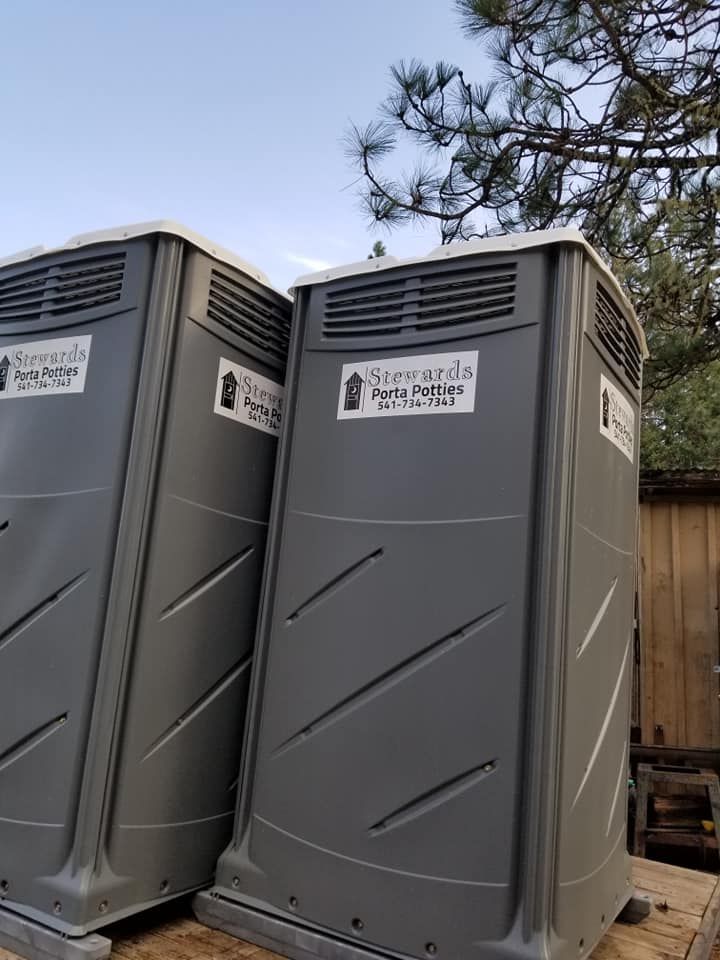 Two gray portable toilets with business logos, outdoors.