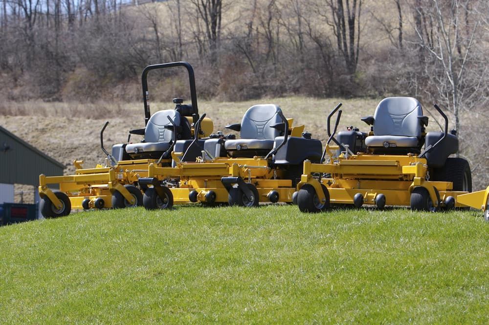 A Row Of Yellow Lawn Mowers Are Parked In A Grassy Field — Eclipse Hire In Cairns, QLD