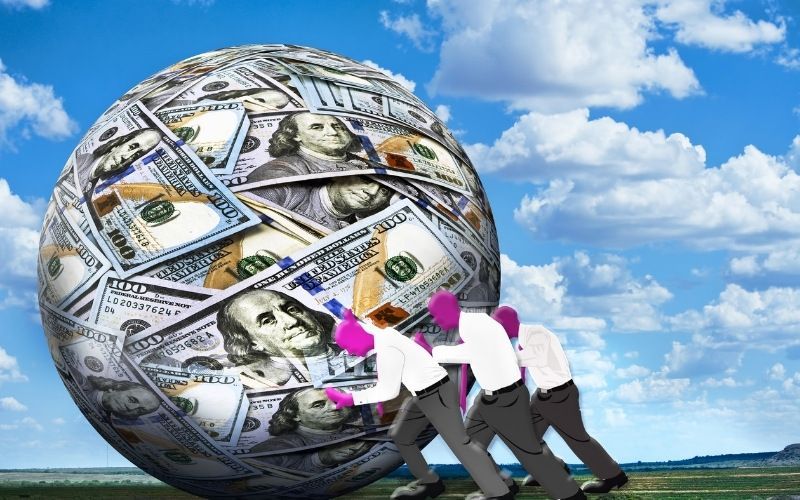 A group of people pushing a ball of money represents the idea of Using the Debt Snowball Method