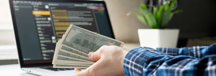 a person is holding a bunch of money in front of a laptop computer emphasizing the idea of Remote Opportunities to Earn a Solid Income