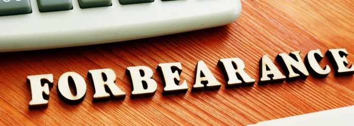 The word forbearance on a wooden table next to a keyboard emphasize the idea of Options for Paused or Reduced Payments.