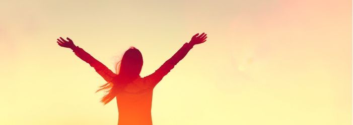 A young woman stands confidently in front of a radiant sunset, symbolizing her journey to regain financial peace and well-being.