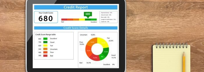 A tablet with a credit report on it is on a wooden table next to a notebook and pencil.