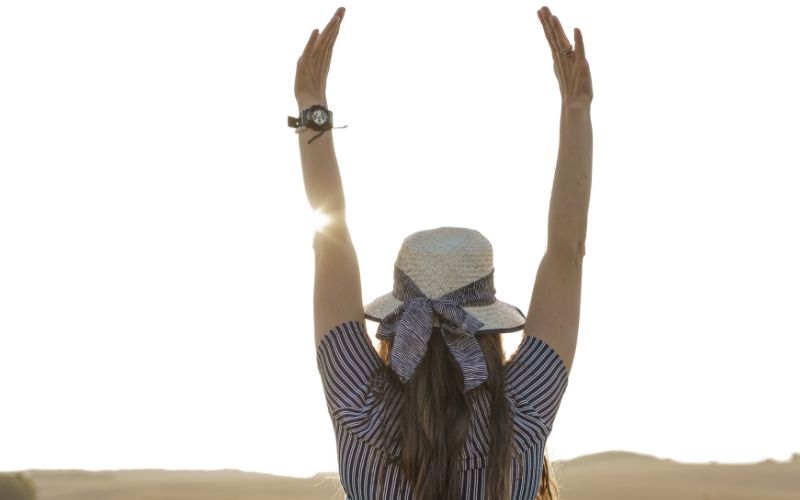 A woman with her back turned, arms raised high, embodies the triumph of conquering financial debt.