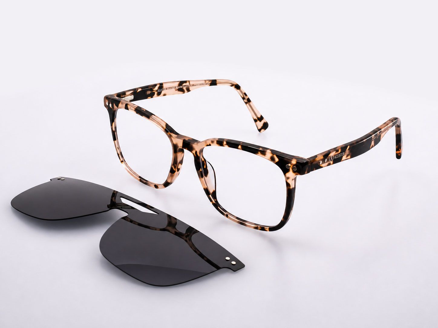 Tortoiseshell eyeglass frames with dark sunglasses lenses beside them on a white background
