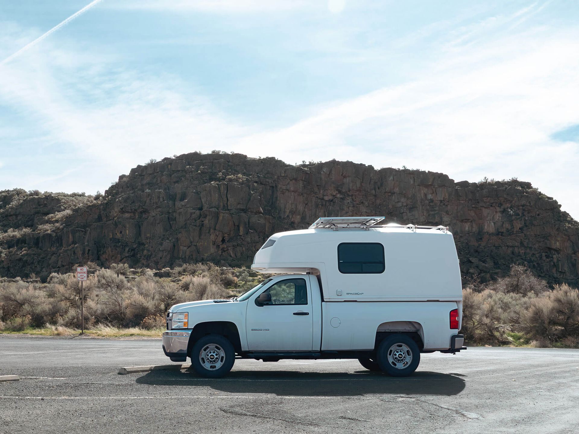White camper truck parked on a roadside with rocky hills in the background under a cloudy sky