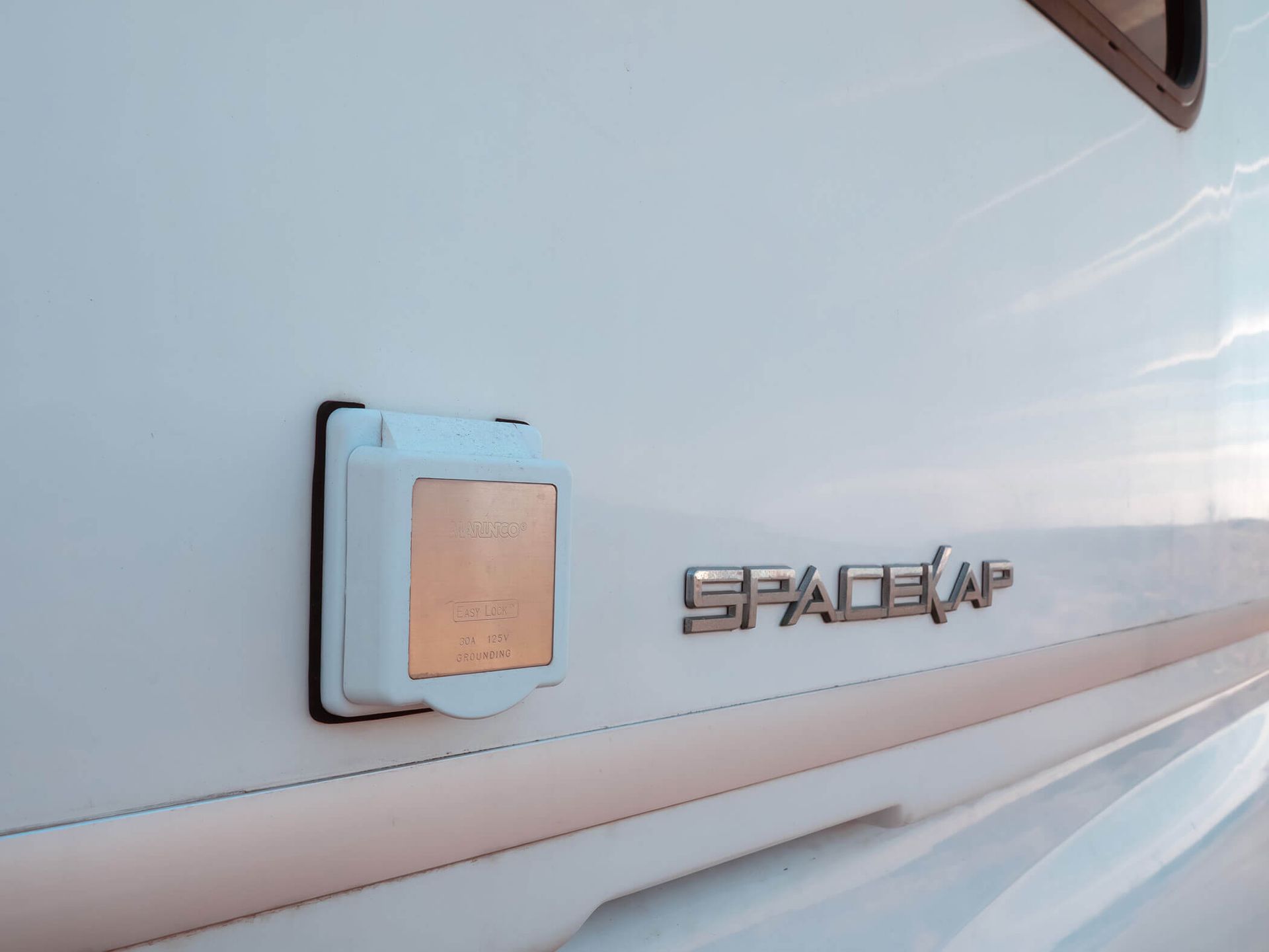 Side view of a white STACIA motorhome with a square charging port and logo on the side