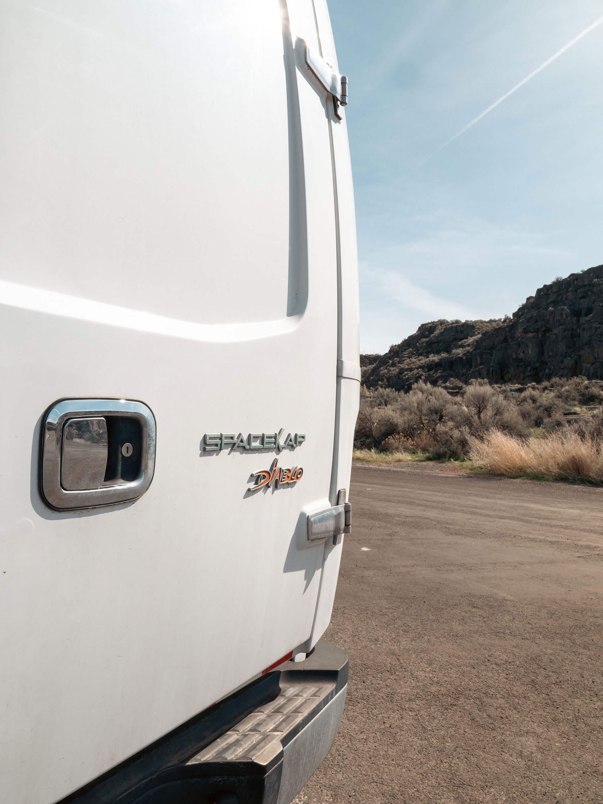 Close-up of a white RV side door with desert landscape and rocky hills in the background