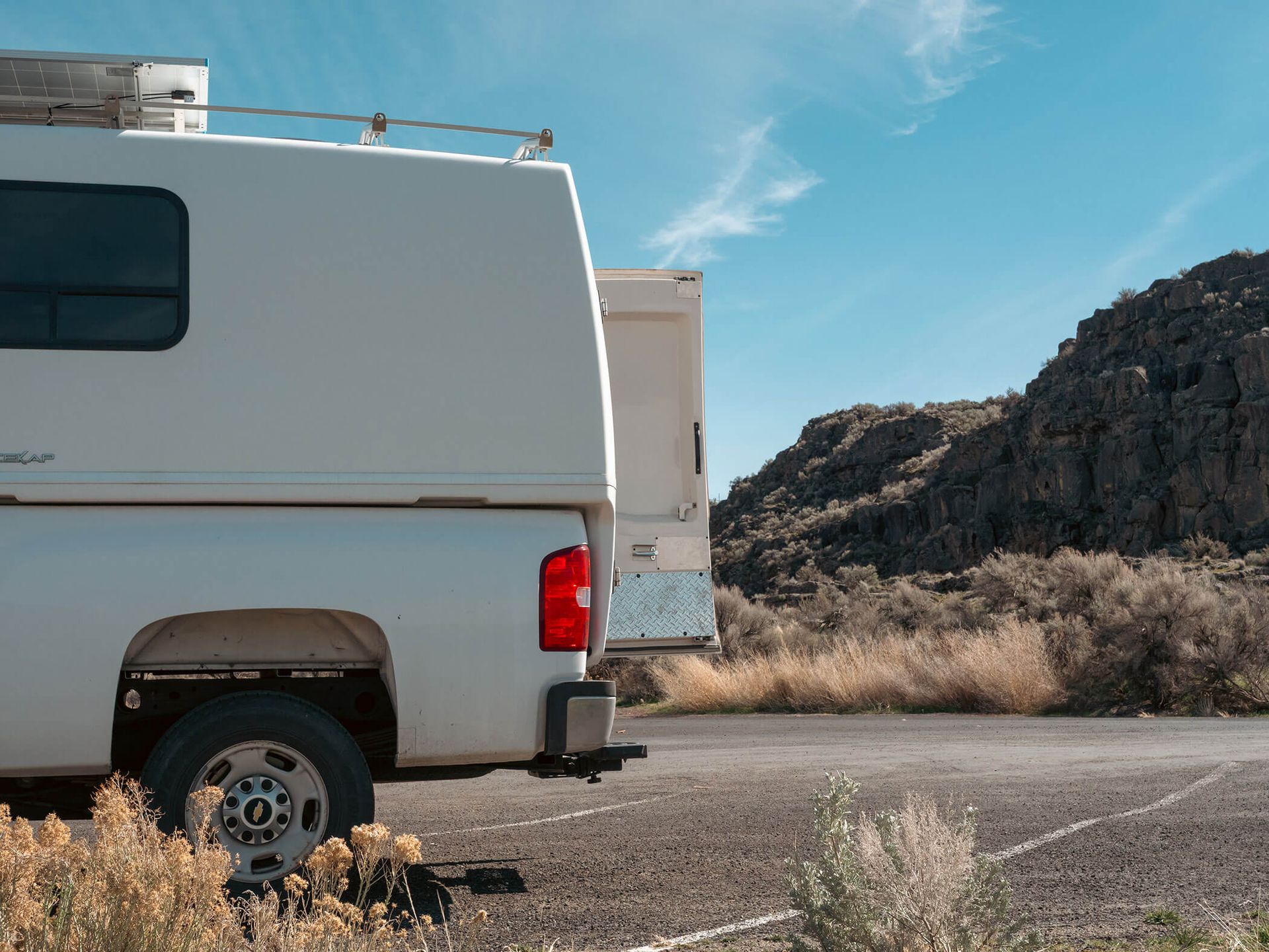 White camper van parked on a desert road beside rocky hills under a blue sky