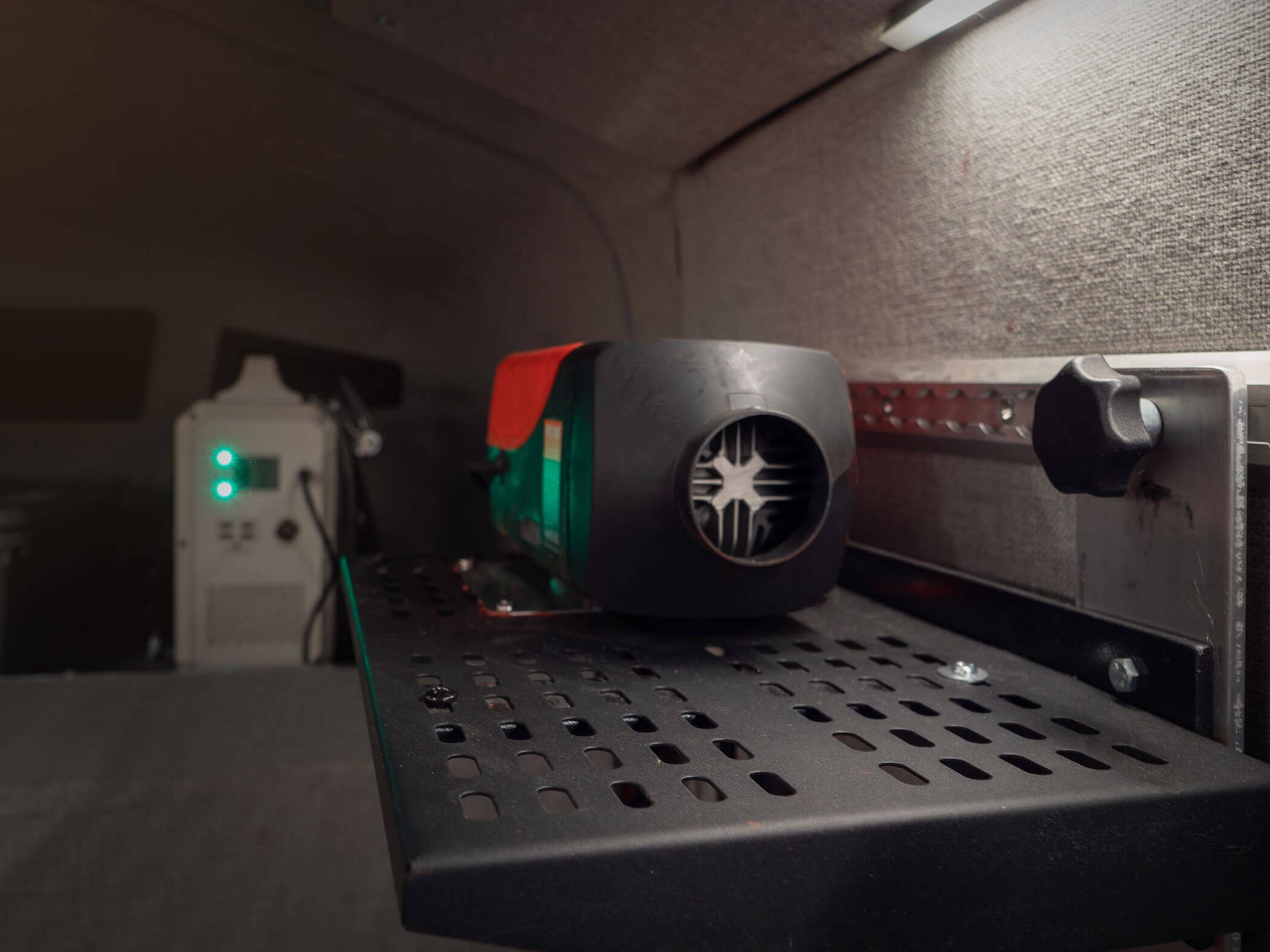 A small robot on a perforated metal shelf inside a cabinet, with wires and a power strip nearby.