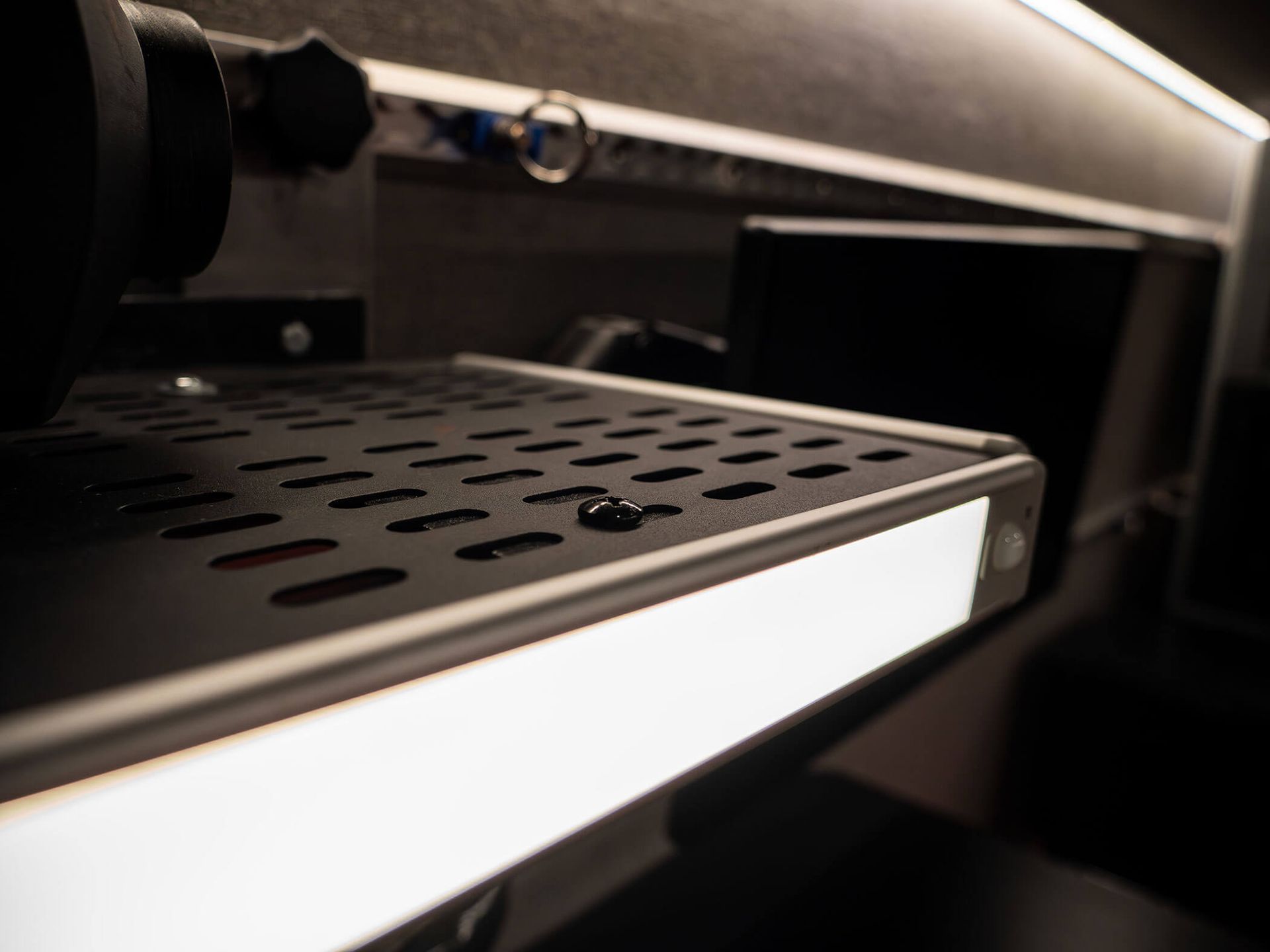 Close-up of a black metal shelf or tray with perforations and a white front edge in a dark cabinet