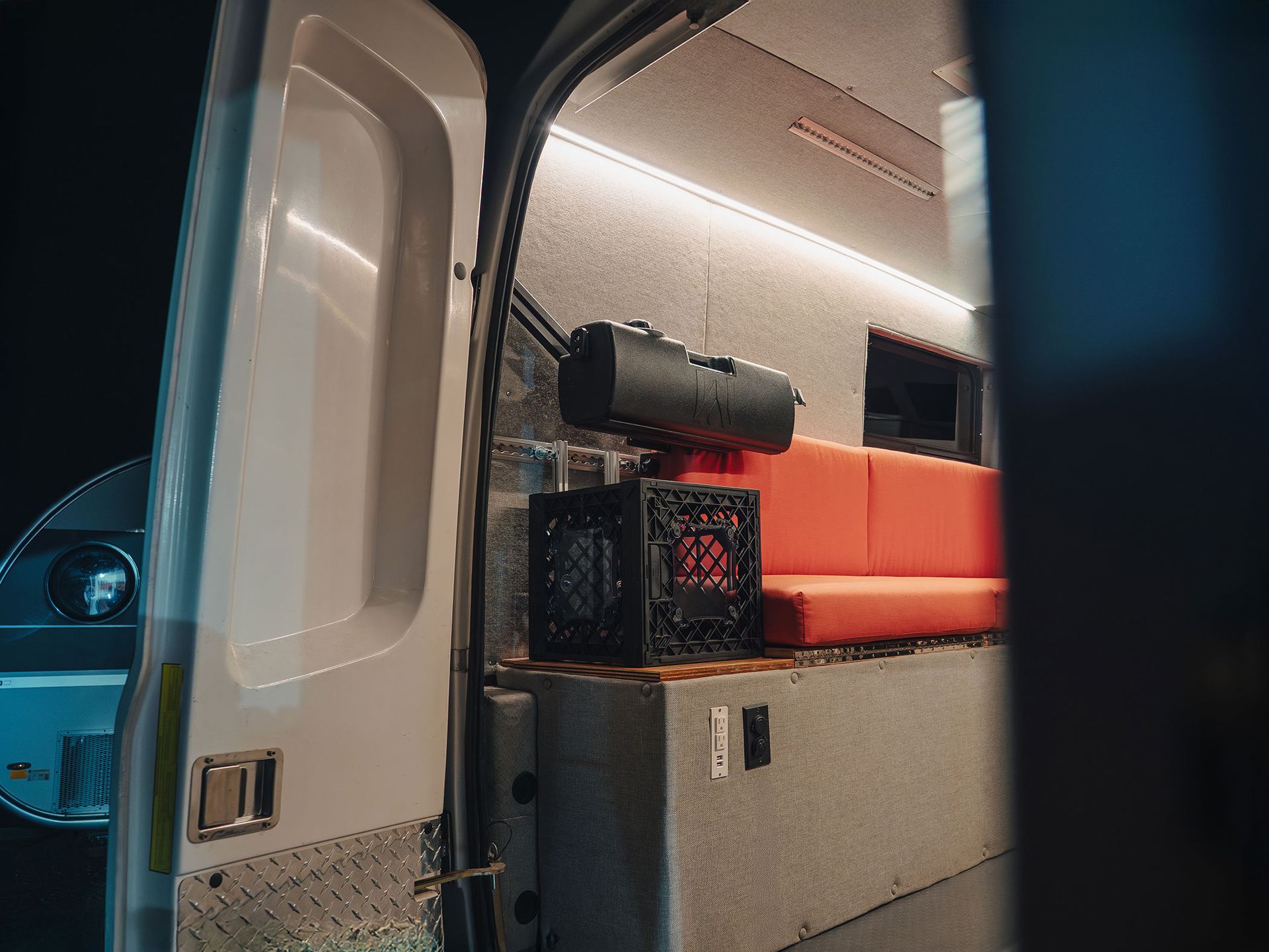 Van interior with orange bench seat, gray storage cabinet, and gear near an open door at night