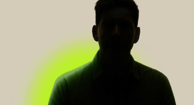 Silhouette of person in a green shirt, face obscured, against a beige background with a green glow.