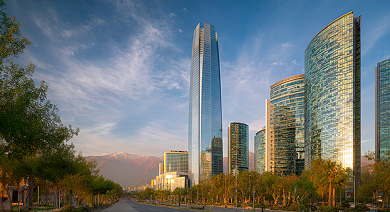 Santiago, Chile skyline with tall, modern skyscrapers. Trees line the foreground, mountains in the distance.