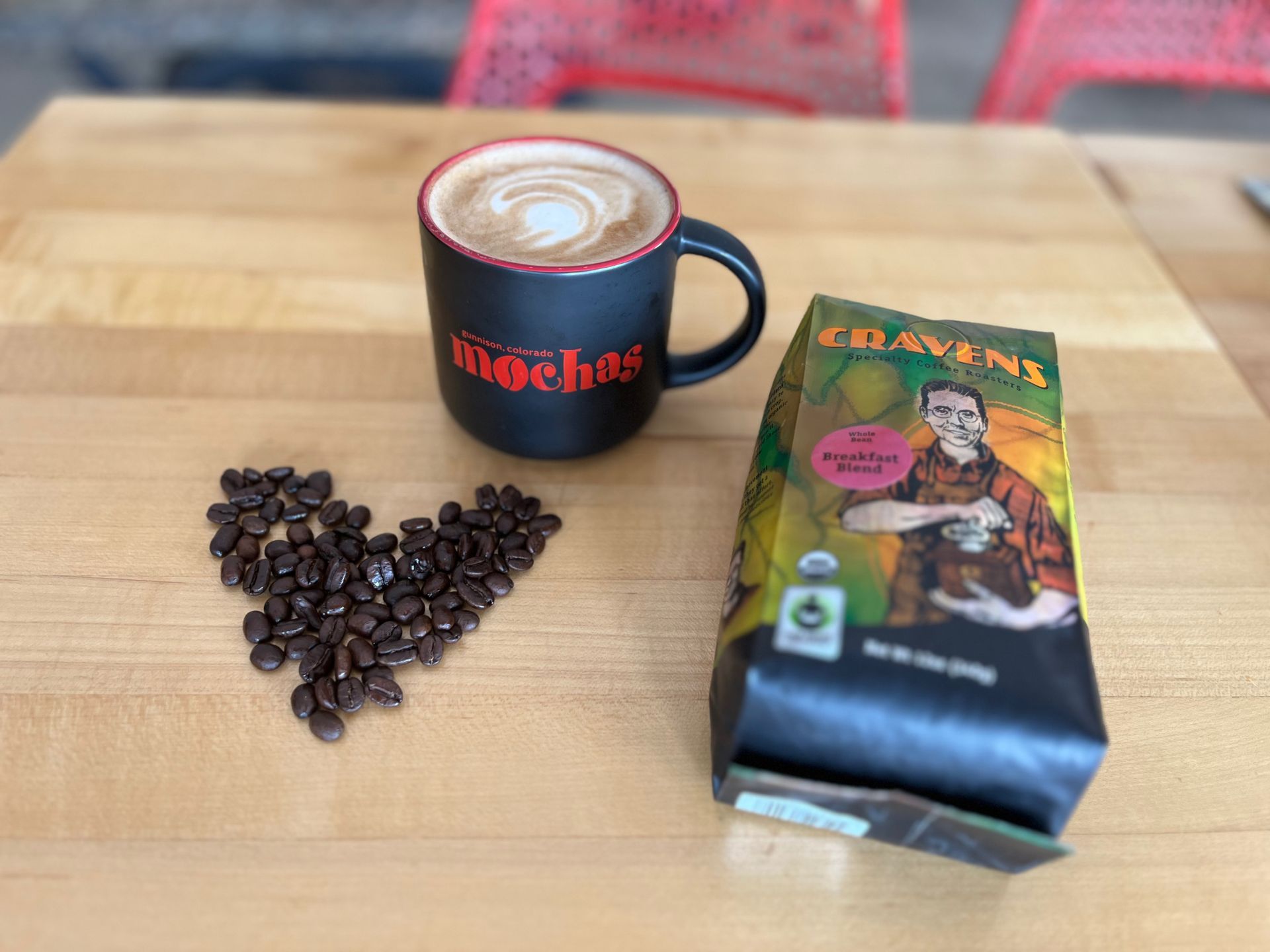 bag of coffee next to cup of coffee and heart coffee beans