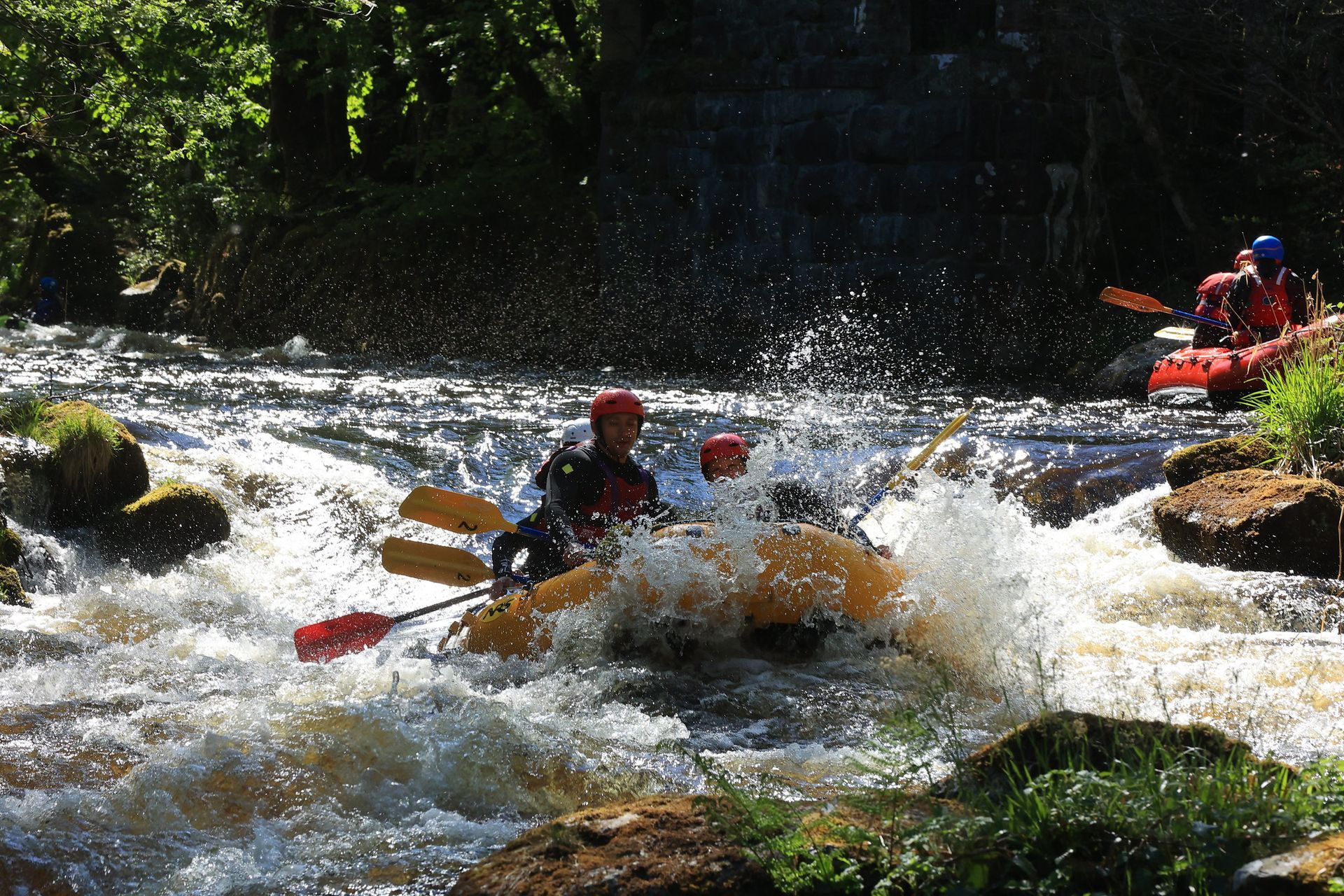 A raft full of happy customers splash through a big rapid on the Afon Tryweryn in the middle of summer
