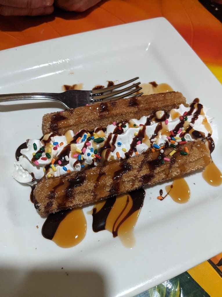 A churro with whipped cream and sprinkles on a plate with a fork