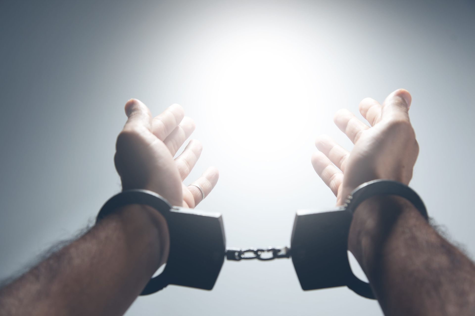 Handcuffed wrists reaching upward toward a bright light