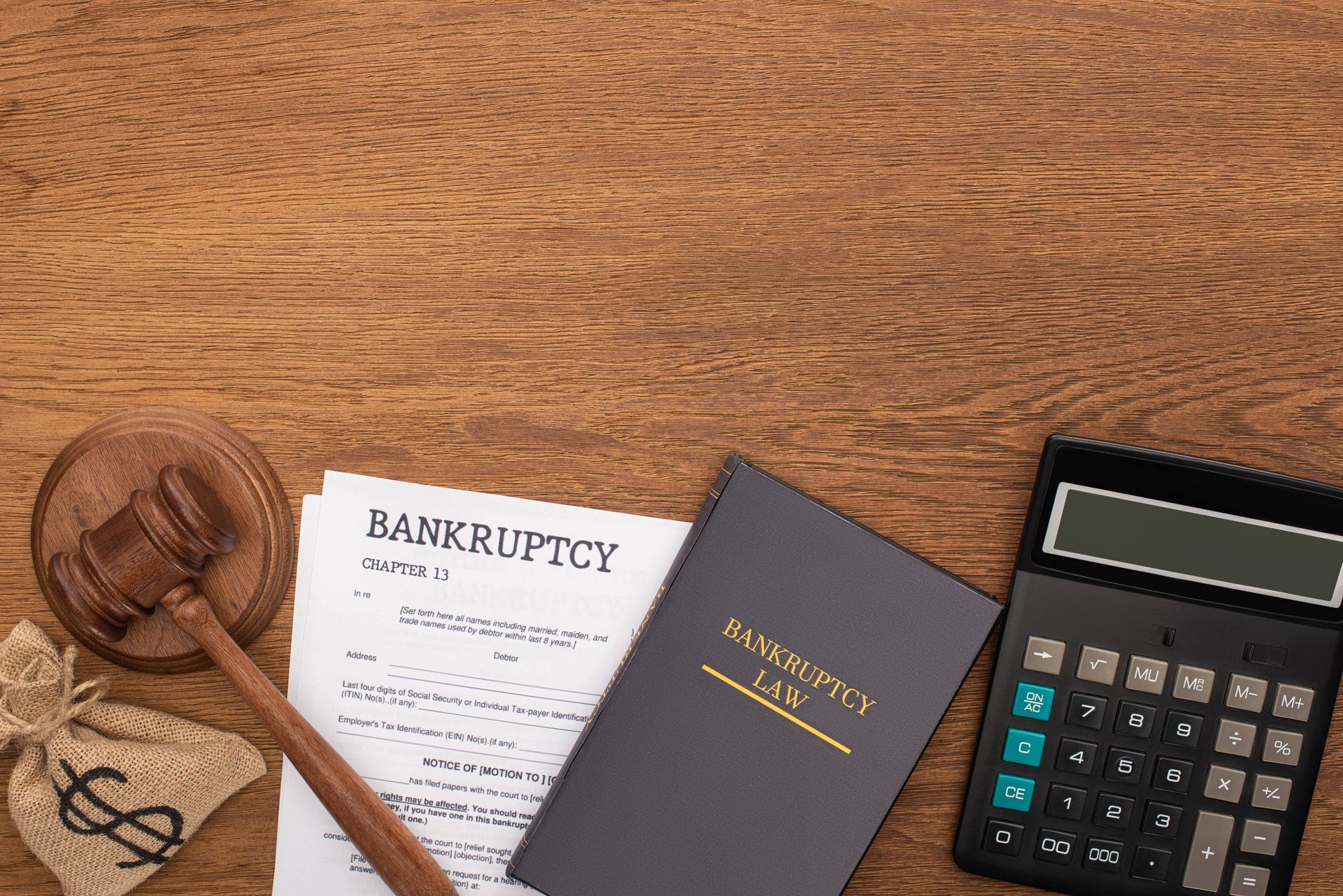 Wooden gavel, bankruptcy documents, law book, money bag, and calculator on a wooden table.