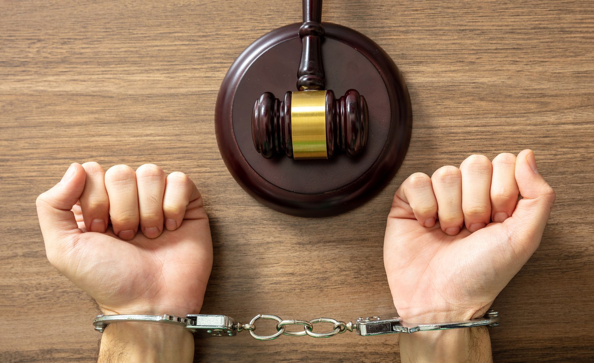 Hands cuffed below a gavel on a wooden surface.