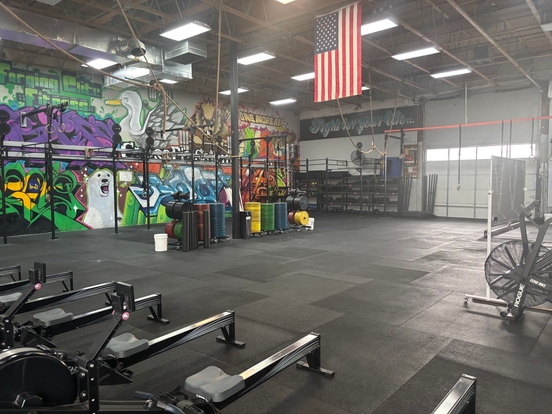 A gym with a row of rowing machines and an american flag hanging from the ceiling.