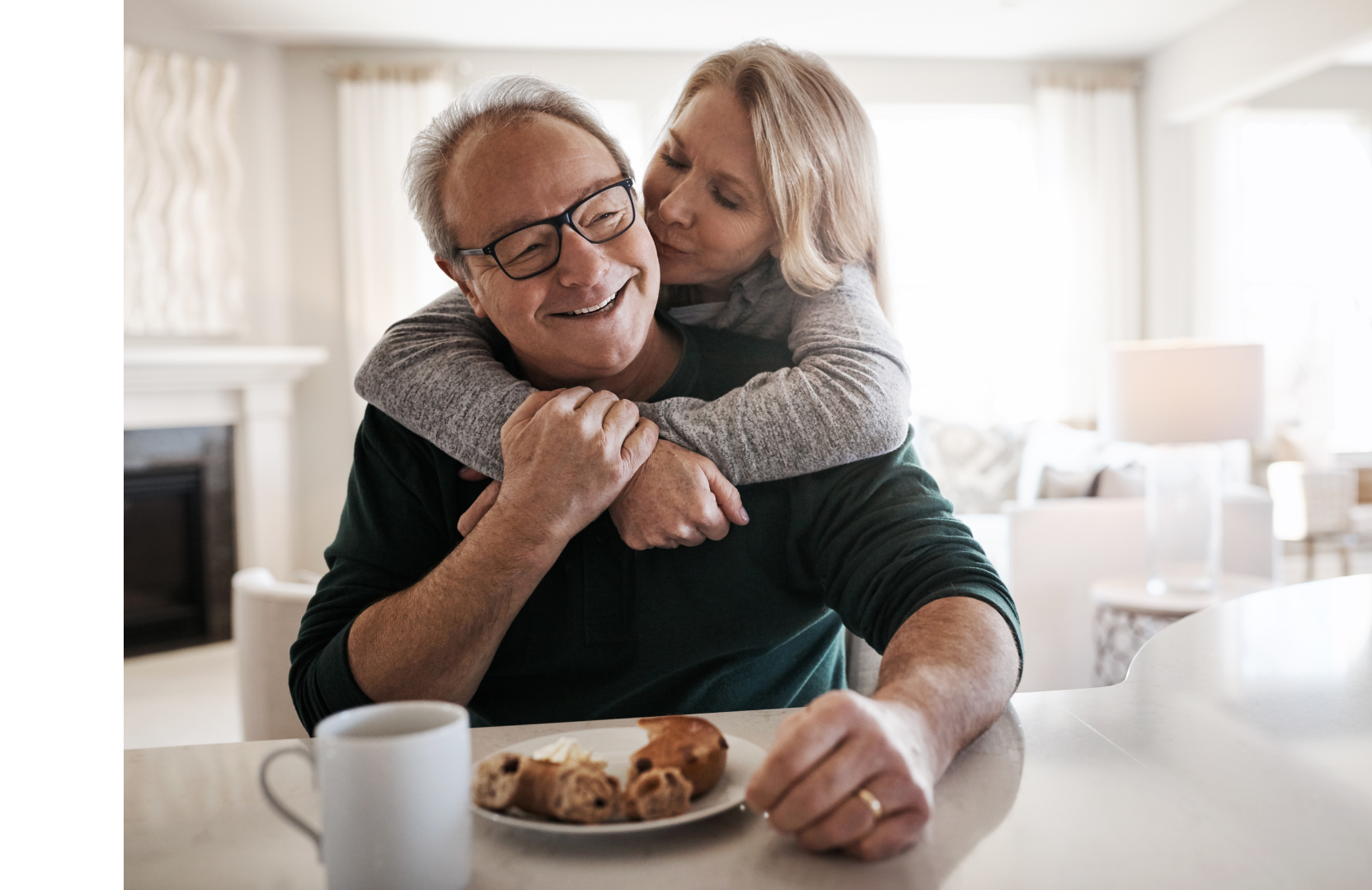 a woman is hugging an older man while sitting at a table with a plate of food .